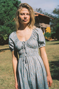 The Brynne Dress in the seasonal Pansy Blues print by Christy Dawn combines delicate femininity with adjustable comfort. It features a low scoop neckline complemented by a drawstring tie at both the neck and waist, allowing a custom fit that enhances your silhouette. Elasticated seams ensure ease of movement, making this dress as practical as it is stylish for versatile wear throughout the season.