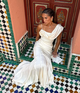 Elevate your elegance with the Celine Satin Dress, a luxurious gown featuring a corset waistline that enhances your silhouette. The design boasts exquisite draping at the hips and a softly flared hemline for graceful movement. A delicate rosette adorns the right shoulder, balanced by a longer, flowing draped scarf on the other, adding refined asymmetry. This sophisticated dress flatters all sizes, making it a timeless choice for any special occasion.