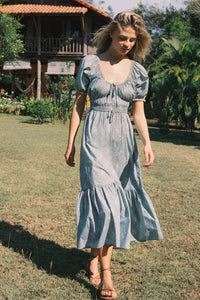 The Brynne Dress in the seasonal Pansy Blues print by Christy Dawn combines delicate femininity with adjustable comfort. It features a low scoop neckline complemented by a drawstring tie at both the neck and waist, allowing a custom fit that enhances your silhouette. Elasticated seams ensure ease of movement, making this dress as practical as it is stylish for versatile wear throughout the season.