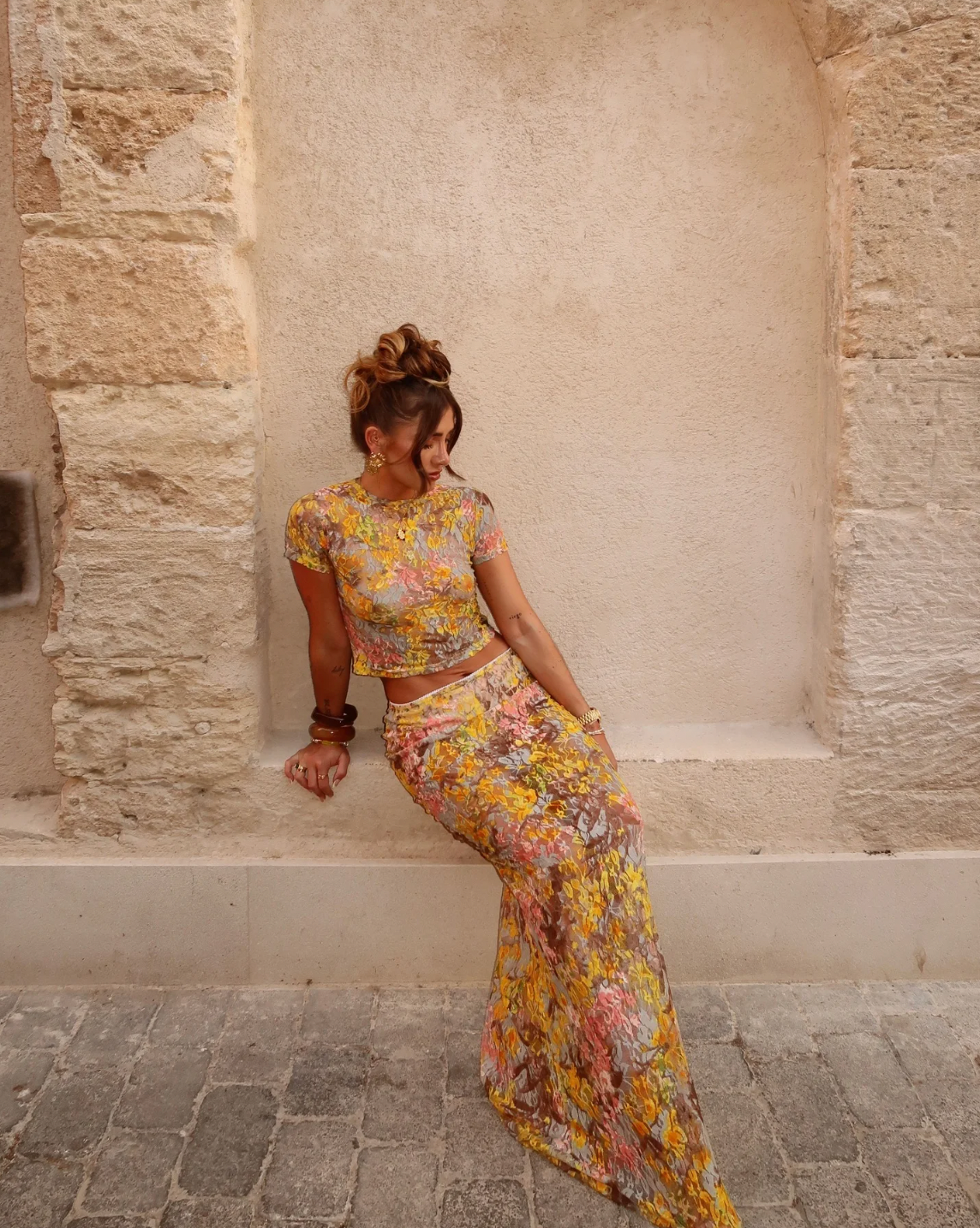 This elegant set features a multi-floral maxi skirt with a form-fitting silhouette that sits mid to low waist, crafted from luxurious stretchy lace for comfort and style. Complemented by a coordinating semi-sheer floral baby t-shirt with cap sleeves and a cropped shape, both pieces showcase a bright summer palette and timeless design, perfect for a sophisticated seasonal look.