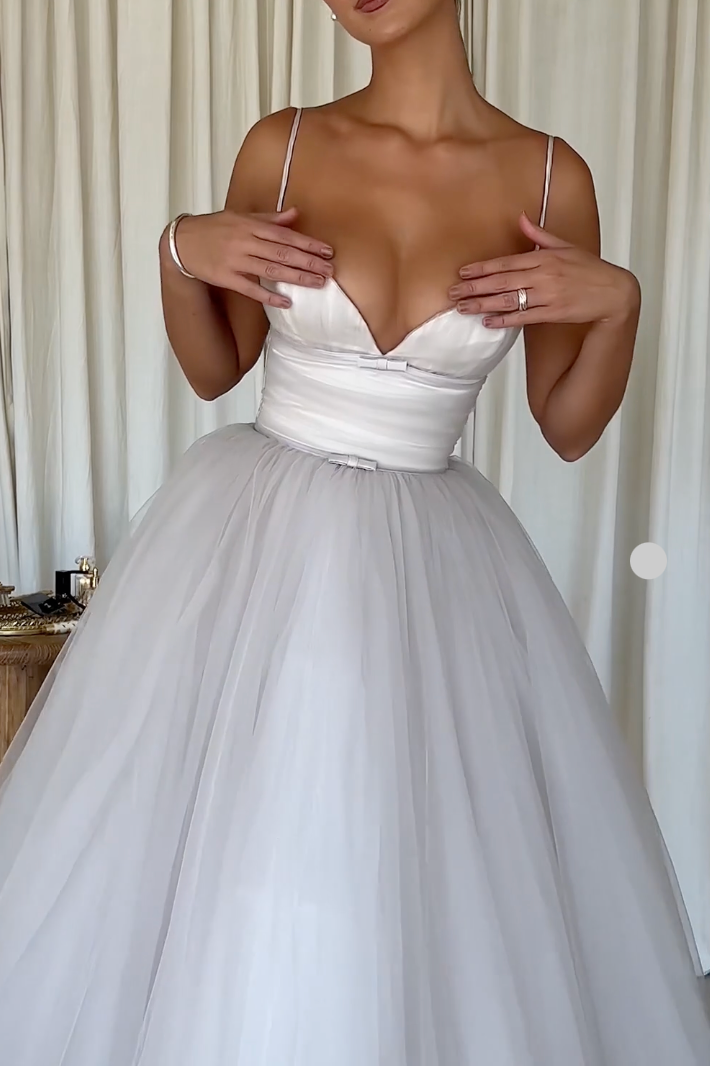 Embrace elegance and playfulness with the French Dove Tulle Dress. This pearlescent midi tulle dress features a plunging neckline and adjustable straps, offering a bespoke fit. The ruched bodice and delicate tulle material are adorned with two small bows for a touch of charm. Feel like a perfect 10 every time you wear it.