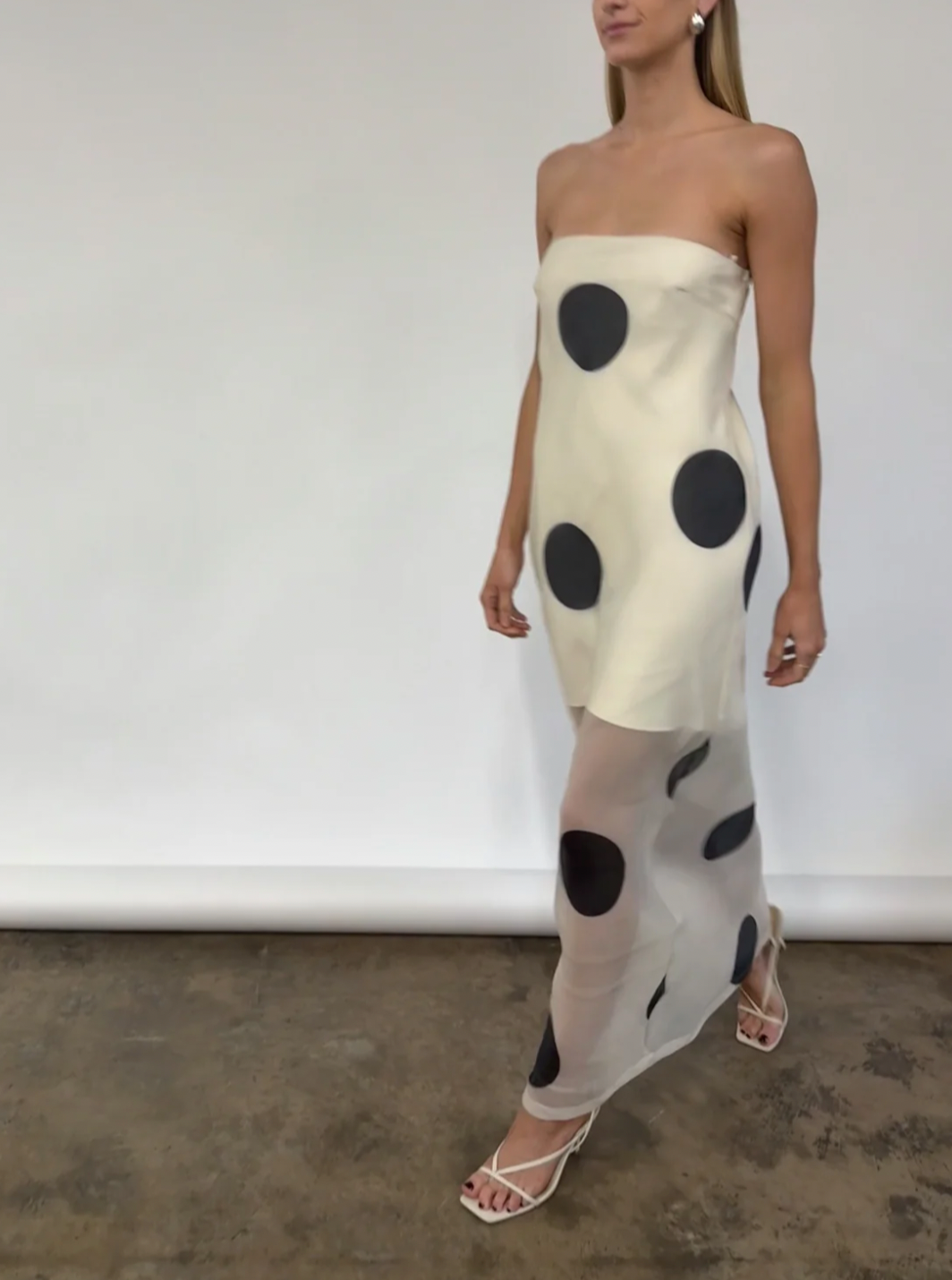 The Mila Maxi Dress in Ivory Polka by Nicole features sheer organza adorned with striking polka dots, shaping a sleek column silhouette. Its half-lined design and elasticated back ensure comfort and adaptability, while the option to wear it with or without straps provides versatile styling choices perfect for refined occasions.