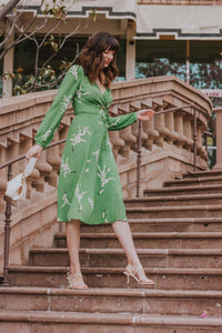 Show off your playful side in the Violette Midi Dress! This stunning lightweight silk dress features a white floral print on a vibrant green background. With 3/4 length sleeves and a comfortable wrap style, you can adjust the waist with the string tie closure. Embrace your love for summer in this unique and stylish dress!