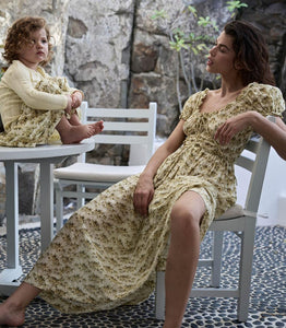 Crafted from soft, lightweight organic cotton voile, the Ashlynn Dress in Citron Rosier Floral by Doen blends Victorian elegance with modern comfort. Featuring short puffed sleeves, a scoop neckline with a functional center tie, and delicate ruffled cuffs, this dress exudes vintage charm. The smocked bodice ensures a flattering fit, complemented by an adjustable waist tie, while the full, ankle-grazing skirt offers graceful movement. Ideal for those seeking refined style with breathable, sustainable fabric.