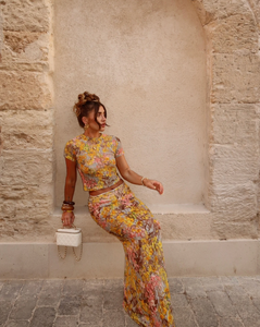 This elegant set features a multi-floral maxi skirt with a form-fitting silhouette that sits mid to low waist, crafted from luxurious stretchy lace for comfort and style. Complemented by a coordinating semi-sheer floral baby t-shirt with cap sleeves and a cropped shape, both pieces showcase a bright summer palette and timeless design, perfect for a sophisticated seasonal look.