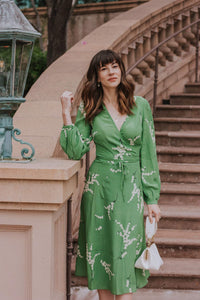 Show off your playful side in the Violette Midi Dress! This stunning lightweight silk dress features a white floral print on a vibrant green background. With 3/4 length sleeves and a comfortable wrap style, you can adjust the waist with the string tie closure. Embrace your love for summer in this unique and stylish dress!