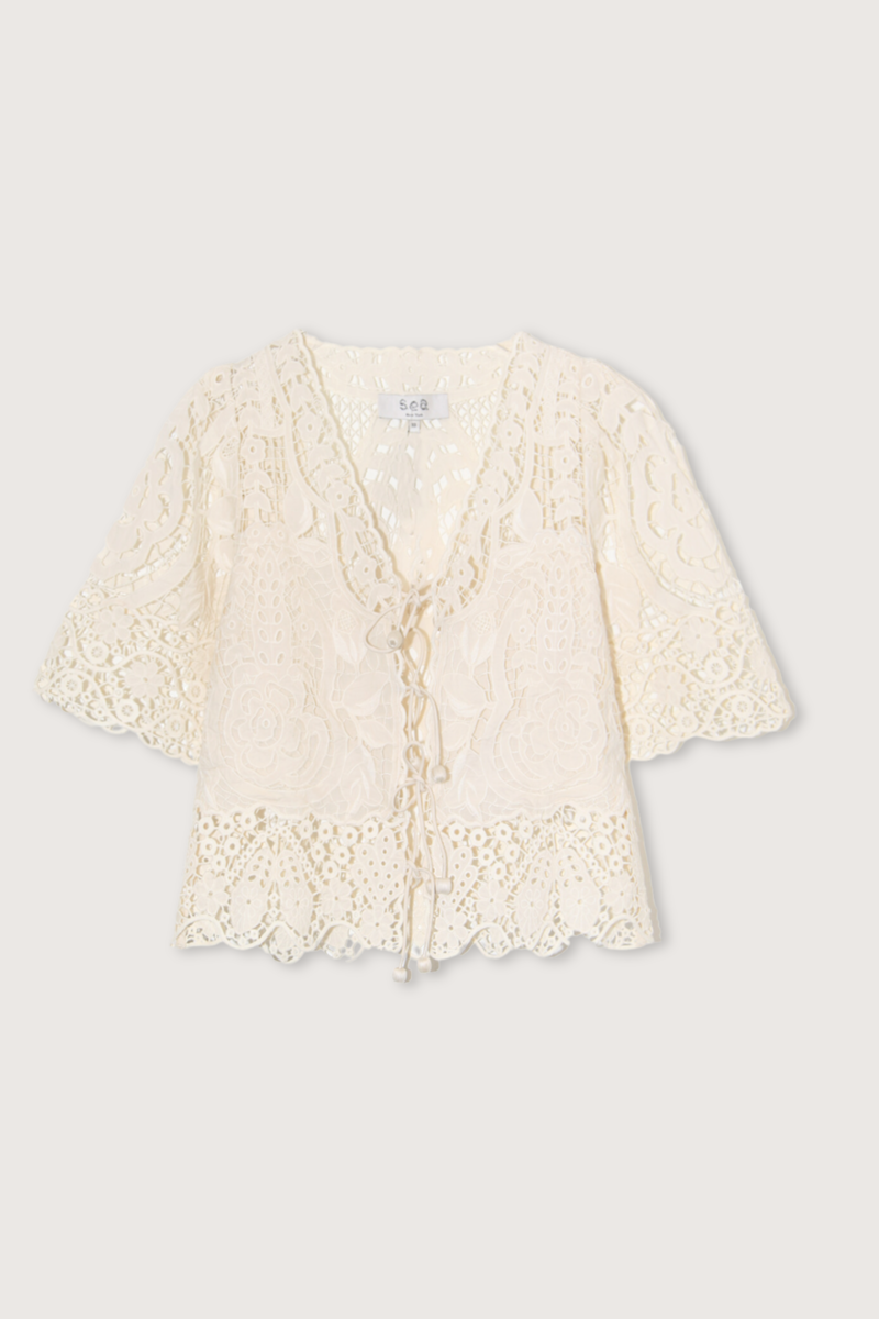 The Gianna Tie Top from Sea New York blends delicate lace detailing with a relaxed fit for effortless elegance. Crafted from 100% cotton with polyester embroidery, it features short flowy sleeves and a front tie closure, delivering both comfort and a romantic silhouette. Ideal for those seeking a refined yet easygoing style.