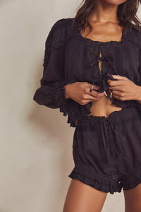 Experience timeless elegance with the Florence Set in Black, designed for both comfort and style. The structured bed jacket features front tie closures, delicate pleated piecing, and banded trumpet sleeves accented by intricate embroidery and ruffle trim. Coordinating shorts offer a drawstring waist for a customizable fit, complemented by ruffle details, pleated patterns, and embroidered accents with a graceful curved hem. Perfect for lounging with refined sophistication.