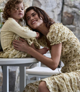 Crafted from soft, lightweight organic cotton voile, the Ashlynn Dress in Citron Rosier Floral by Doen blends Victorian elegance with modern comfort. Featuring short puffed sleeves, a scoop neckline with a functional center tie, and delicate ruffled cuffs, this dress exudes vintage charm. The smocked bodice ensures a flattering fit, complemented by an adjustable waist tie, while the full, ankle-grazing skirt offers graceful movement. Ideal for those seeking refined style with breathable, sustainable fabric.