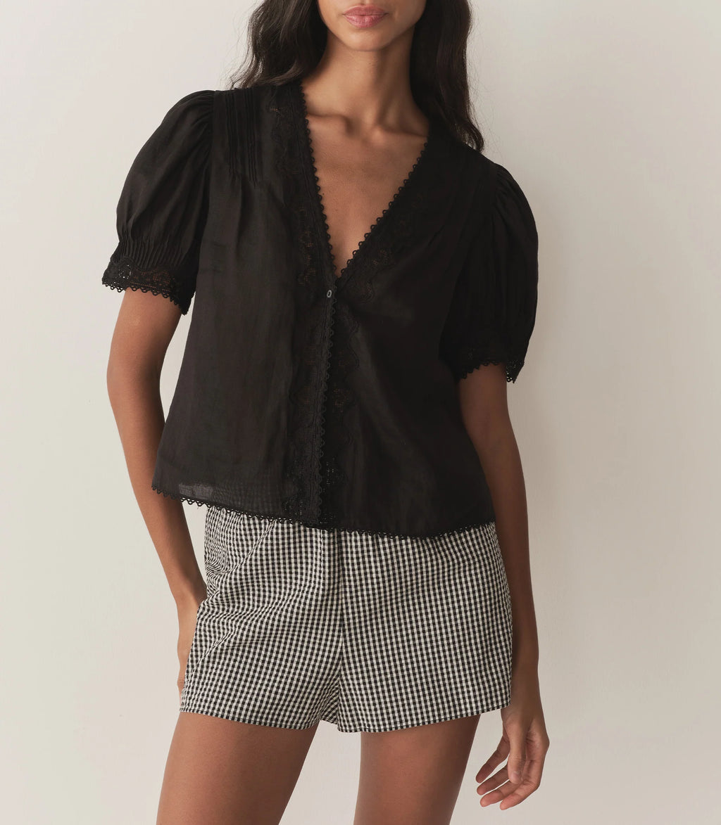 Crafted from lightweight semi-sheer ramie, the Brigitta Top by Doen draws inspiration from Victorian fashion with its plunging V-neckline and delicate lace detailing. The short puffed sleeves feature clustered pintucks, while a line of starburst buttons runs down the center front, adding refined charm. Versatile in style, it can be worn loose for an airy feel or tucked into high-waisted jeans for a polished look.