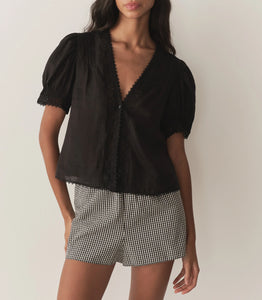 Crafted from lightweight semi-sheer ramie, the Brigitta Top by Doen draws inspiration from Victorian fashion with its plunging V-neckline and delicate lace detailing. The short puffed sleeves feature clustered pintucks, while a line of starburst buttons runs down the center front, adding refined charm. Versatile in style, it can be worn loose for an airy feel or tucked into high-waisted jeans for a polished look.