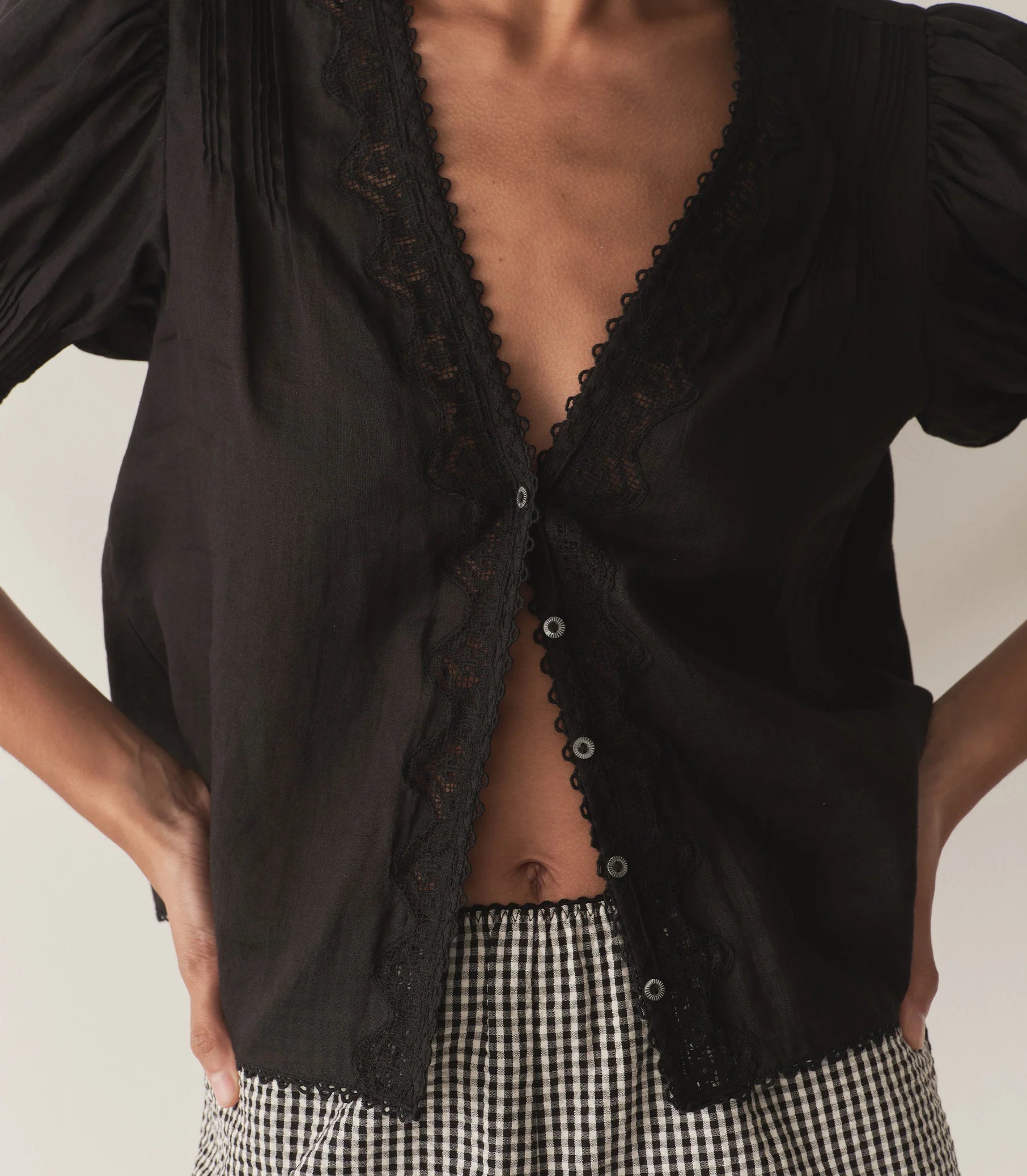 Crafted from lightweight semi-sheer ramie, the Brigitta Top by Doen draws inspiration from Victorian fashion with its plunging V-neckline and delicate lace detailing. The short puffed sleeves feature clustered pintucks, while a line of starburst buttons runs down the center front, adding refined charm. Versatile in style, it can be worn loose for an airy feel or tucked into high-waisted jeans for a polished look.