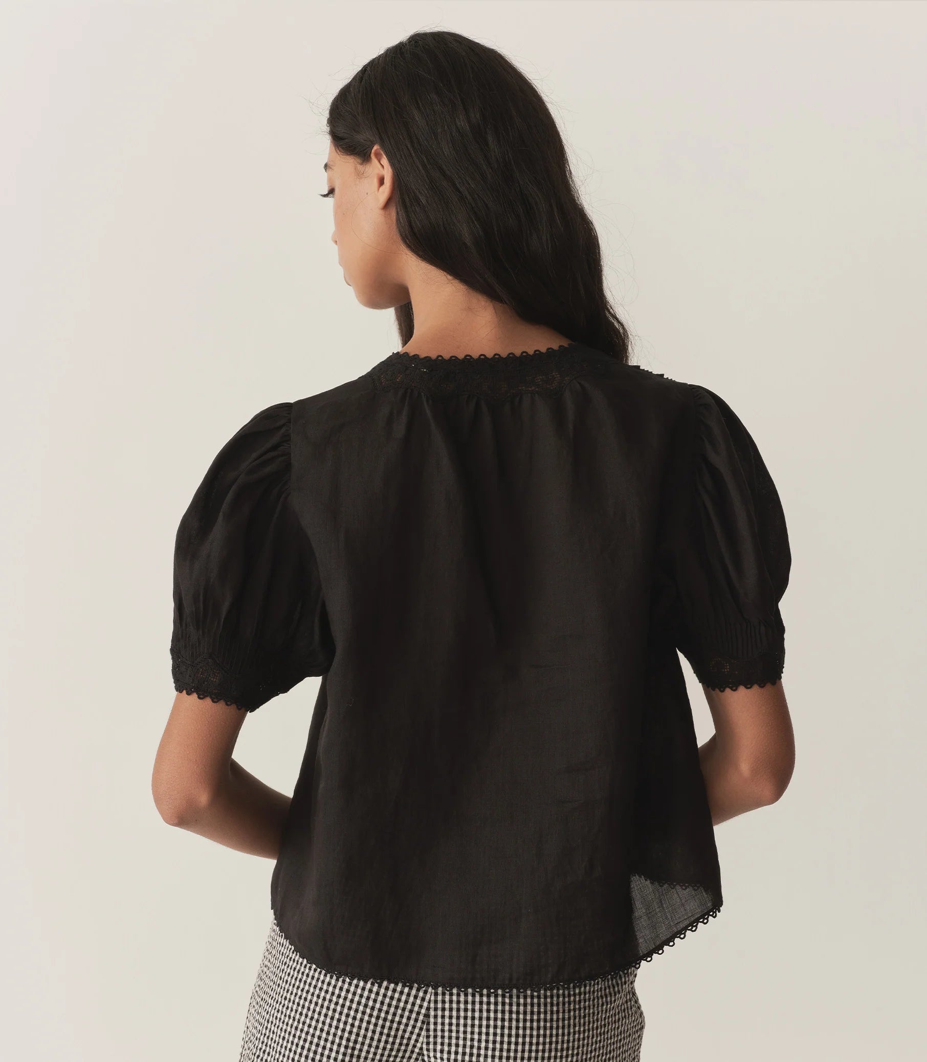 Crafted from lightweight semi-sheer ramie, the Brigitta Top by Doen draws inspiration from Victorian fashion with its plunging V-neckline and delicate lace detailing. The short puffed sleeves feature clustered pintucks, while a line of starburst buttons runs down the center front, adding refined charm. Versatile in style, it can be worn loose for an airy feel or tucked into high-waisted jeans for a polished look.