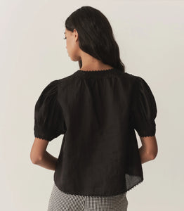 Crafted from lightweight semi-sheer ramie, the Brigitta Top by Doen draws inspiration from Victorian fashion with its plunging V-neckline and delicate lace detailing. The short puffed sleeves feature clustered pintucks, while a line of starburst buttons runs down the center front, adding refined charm. Versatile in style, it can be worn loose for an airy feel or tucked into high-waisted jeans for a polished look.