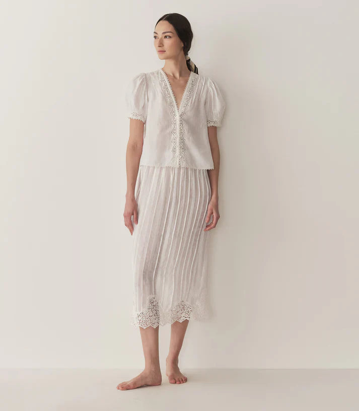 Crafted from lightweight semi-sheer ramie, the Brigitta Top by Doen draws inspiration from Victorian fashion with its plunging V-neckline and delicate lace detailing. The short puffed sleeves feature clustered pintucks, while a line of starburst buttons runs down the center front, adding refined charm. Versatile in style, it can be worn loose for an airy feel or tucked into high-waisted jeans for a polished look.