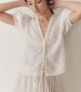 Crafted from lightweight semi-sheer ramie, the Brigitta Top by Doen draws inspiration from Victorian fashion with its plunging V-neckline and delicate lace detailing. The short puffed sleeves feature clustered pintucks, while a line of starburst buttons runs down the center front, adding refined charm. Versatile in style, it can be worn loose for an airy feel or tucked into high-waisted jeans for a polished look.