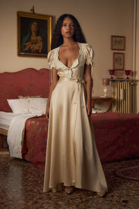 Crafted from luxurious silk charmeuse, the Unwrap Me Gown in Crème features delicate lace trim along the neckline and sleeves, enhancing its refined silhouette. Lace-covered buttons with hidden snaps offer elegant closure at the center front, while a matching silk charmeuse belt with chain stitch loops and snaps defines the waist. An adjustable slit secured by hook and thread loops adds both comfort and sophistication, making this gown a masterful blend of exquisite detail and expert tailoring.