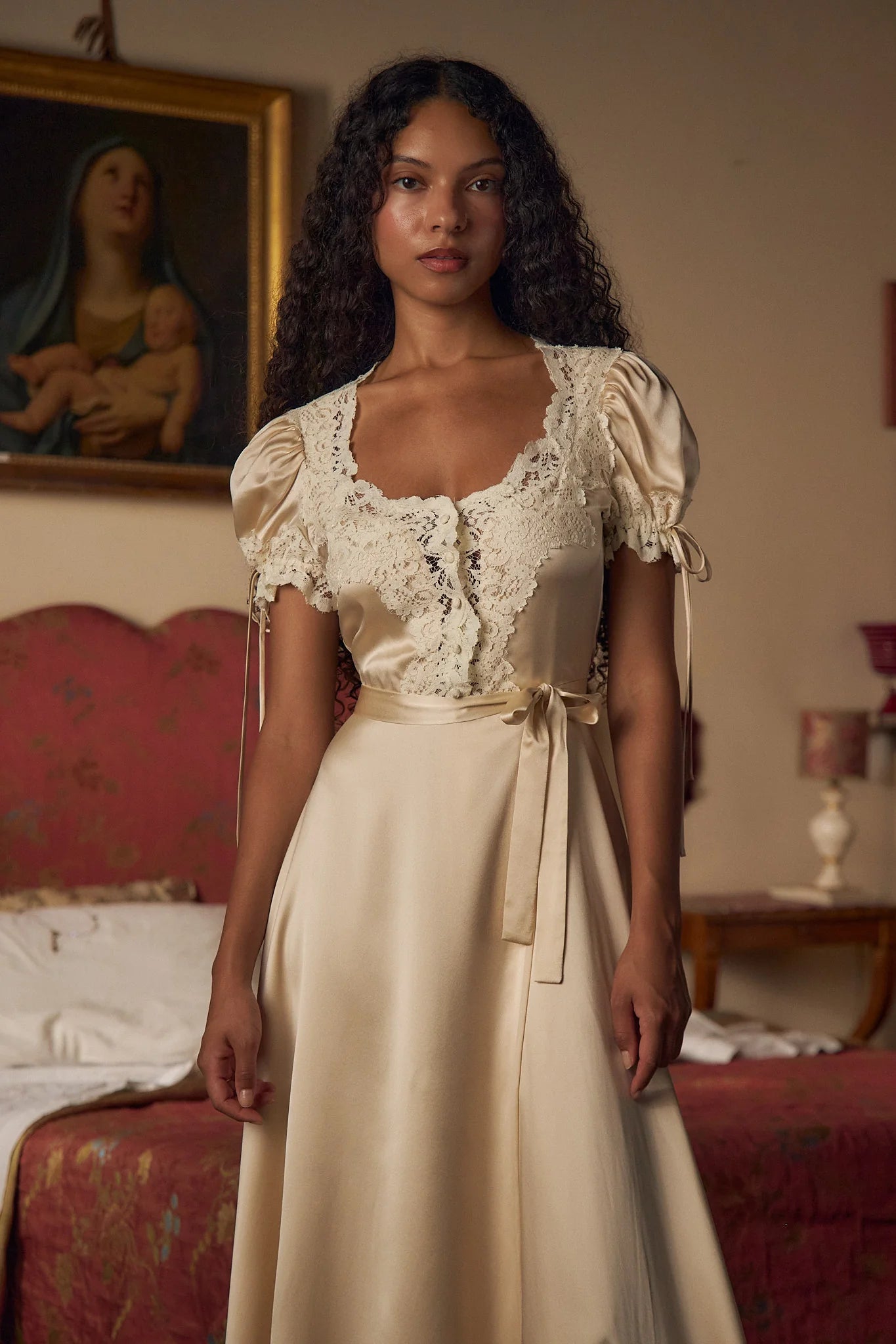 Crafted from luxurious silk charmeuse, the Unwrap Me Gown in Crème features delicate lace trim along the neckline and sleeves, enhancing its refined silhouette. Lace-covered buttons with hidden snaps offer elegant closure at the center front, while a matching silk charmeuse belt with chain stitch loops and snaps defines the waist. An adjustable slit secured by hook and thread loops adds both comfort and sophistication, making this gown a masterful blend of exquisite detail and expert tailoring.