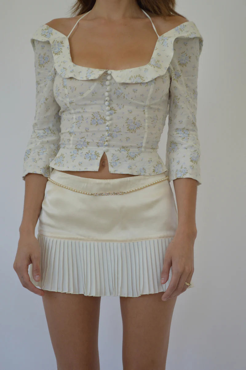 Crafted from 100% organic cotton, the Margot Top in Vintage Iris by Fait Par Foutch offers a refined blend of comfort and elegance. Its adjustable lacing at the back ensures a tailored fit, complemented by delicate fold-over collar detailing and subtle non-functional buttons along the center front. Interior French seams enhance durability and a polished finish, while adjustable halter ties provide versatile styling options. 
