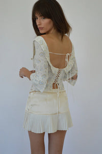 Crafted from 100% organic cotton, the Margot Top in Vintage Iris by Fait Par Foutch offers a refined blend of comfort and elegance. Its adjustable lacing at the back ensures a tailored fit, complemented by delicate fold-over collar detailing and subtle non-functional buttons along the center front. Interior French seams enhance durability and a polished finish, while adjustable halter ties provide versatile styling options. 