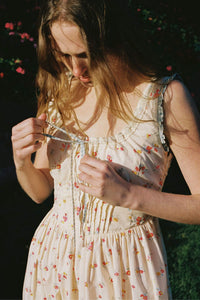Inspired by Edwardian corsets, the Eliana Dress combines classic sophistication with contemporary ease. Made from 100% organic cotton, this sleeveless midi features an exaggerated wide scoop neckline adorned with contrasting eyelet trim and soft ruffles. A half-functional front button placket and subtle micro pintucks at the bust provide elegant accents, while the lace-up back creates a striking, form-fitting silhouette. 