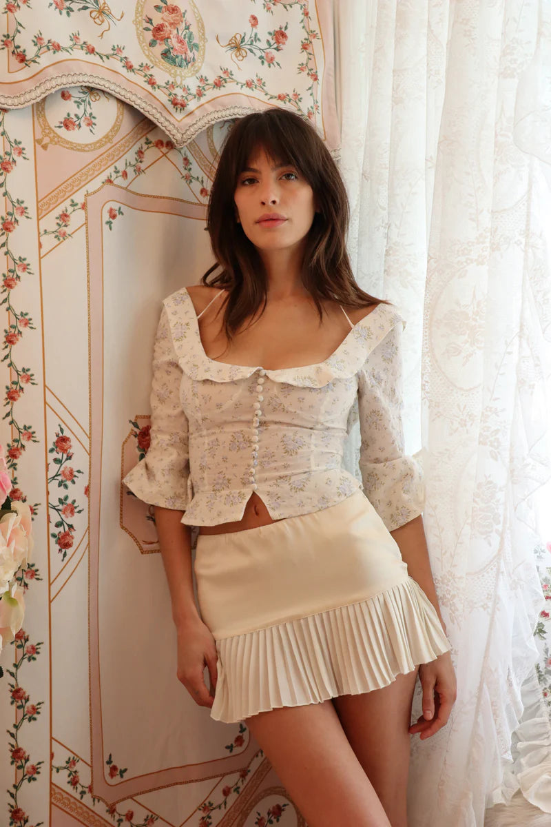 Crafted from 100% organic cotton, the Margot Top in Vintage Iris by Fait Par Foutch offers a refined blend of comfort and elegance. Its adjustable lacing at the back ensures a tailored fit, complemented by delicate fold-over collar detailing and subtle non-functional buttons along the center front. Interior French seams enhance durability and a polished finish, while adjustable halter ties provide versatile styling options. 