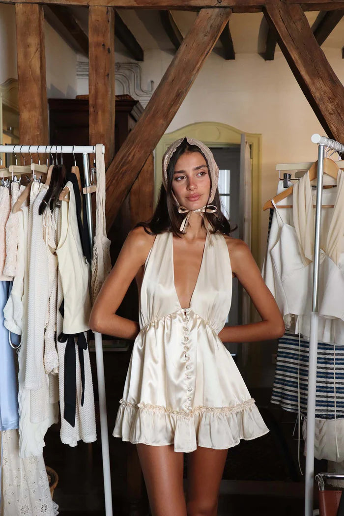 The Caroline Dress by Fait par Foutch is crafted from medium-weight 100% silk charmeuse, offering a luxurious, smooth texture that drapes elegantly. Fully lined with pure silk for enhanced comfort, it features functional silk-covered buttons and loops down the center front. Its low V-neckline and halter straps tie into an adjustable bow at the neck, providing a customizable fit. The low back design includes hidden elastic at the waist, ensuring a flattering silhouette and secure fit. 