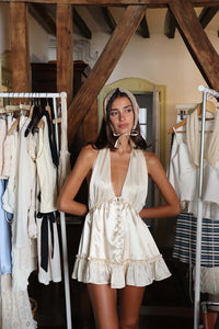 The Caroline Dress by Fait par Foutch is crafted from medium-weight 100% silk charmeuse, offering a luxurious, smooth texture that drapes elegantly. Fully lined with pure silk for enhanced comfort, it features functional silk-covered buttons and loops down the center front. Its low V-neckline and halter straps tie into an adjustable bow at the neck, providing a customizable fit. The low back design includes hidden elastic at the waist, ensuring a flattering silhouette and secure fit. 