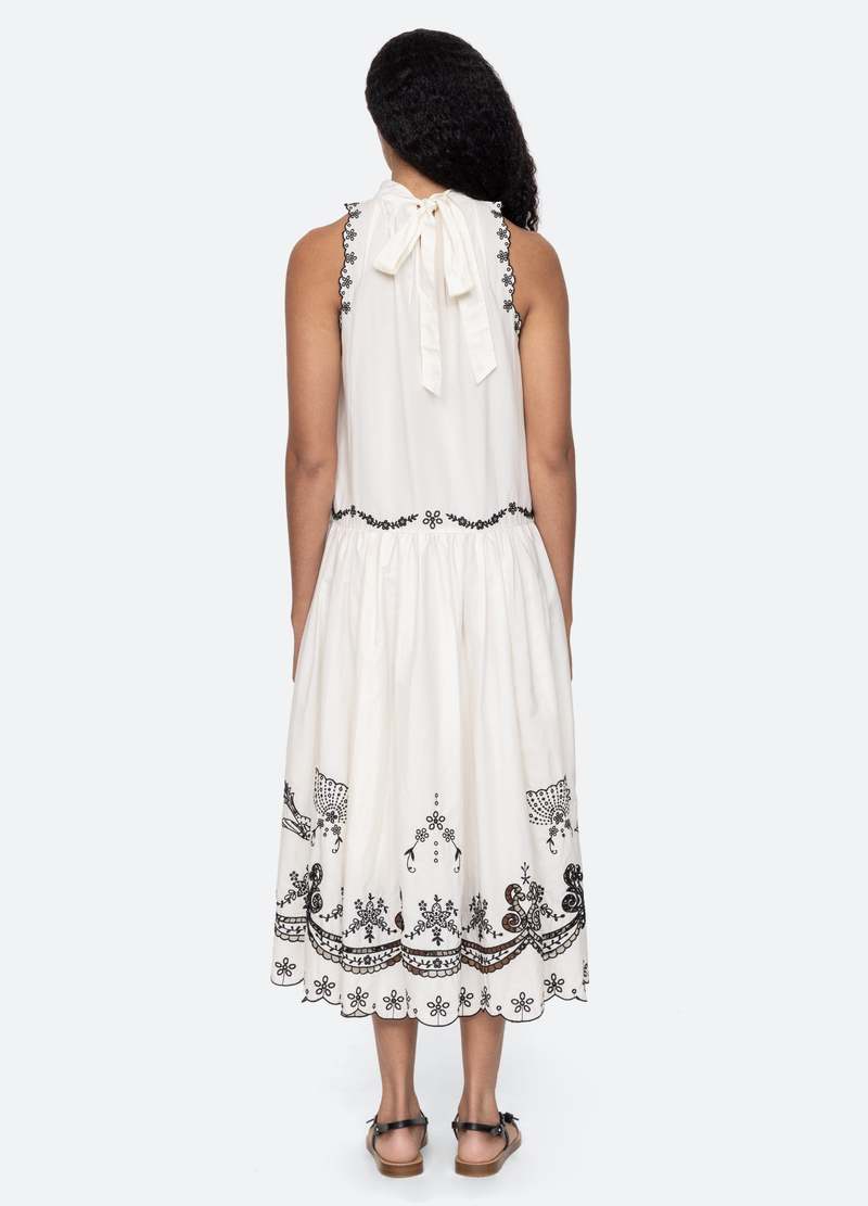 The Kingsley embroidered tank dress in cream by SEA NY showcases intricate embroidery throughout its design, offering a refined and elegant appeal. It features a high neckline that adds a sophisticated touch, complemented by a delicate back bow tie for adjustable fit and added charm. The scalloped hemline enhances the dress's feminine silhouette, making it an exceptional choice for those seeking a polished yet distinctive look.
