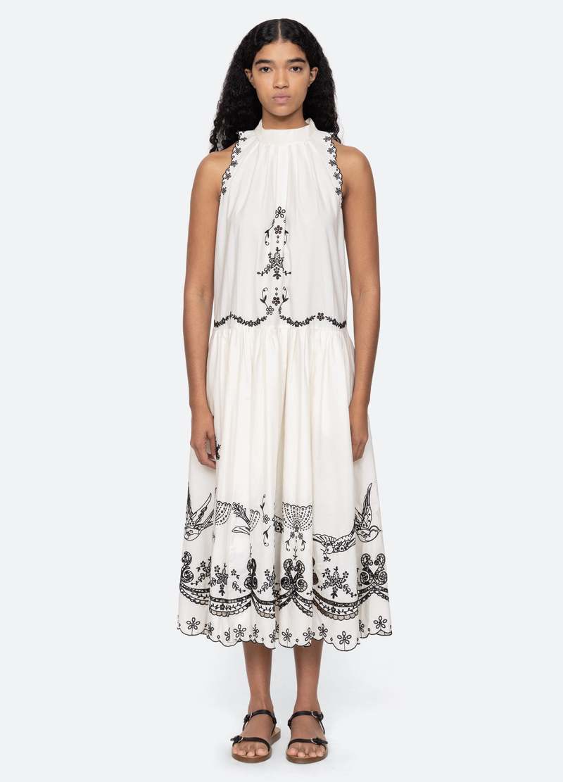 The Kingsley embroidered tank dress in cream by SEA NY showcases intricate embroidery throughout its design, offering a refined and elegant appeal. It features a high neckline that adds a sophisticated touch, complemented by a delicate back bow tie for adjustable fit and added charm. The scalloped hemline enhances the dress's feminine silhouette, making it an exceptional choice for those seeking a polished yet distinctive look.