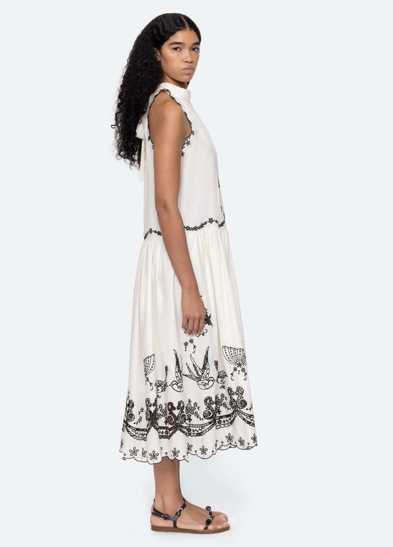 The Kingsley embroidered tank dress in cream by SEA NY showcases intricate embroidery throughout its design, offering a refined and elegant appeal. It features a high neckline that adds a sophisticated touch, complemented by a delicate back bow tie for adjustable fit and added charm. The scalloped hemline enhances the dress's feminine silhouette, making it an exceptional choice for those seeking a polished yet distinctive look.