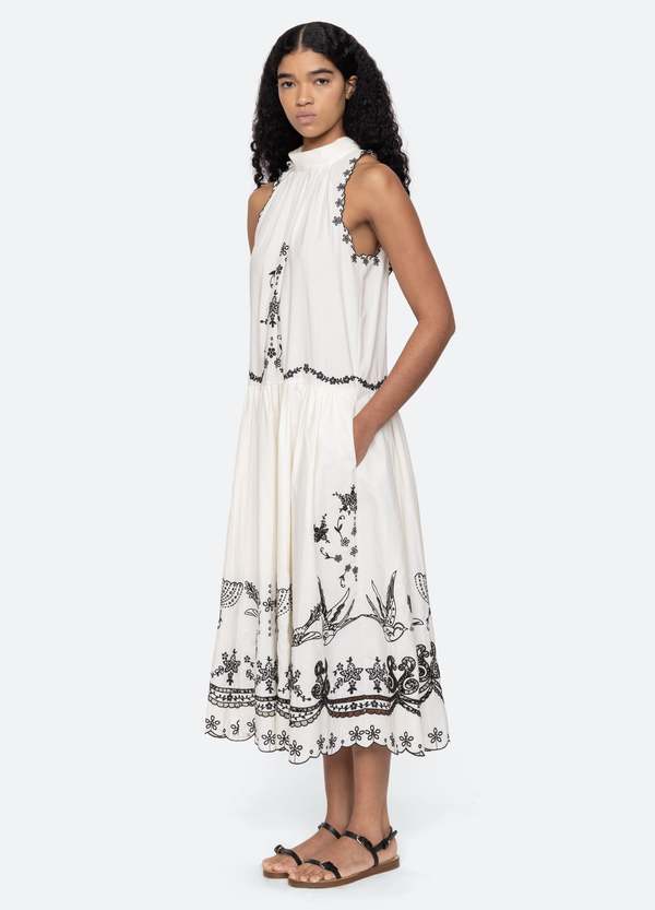 The Kingsley embroidered tank dress in cream by SEA NY showcases intricate embroidery throughout its design, offering a refined and elegant appeal. It features a high neckline that adds a sophisticated touch, complemented by a delicate back bow tie for adjustable fit and added charm. The scalloped hemline enhances the dress's feminine silhouette, making it an exceptional choice for those seeking a polished yet distinctive look.