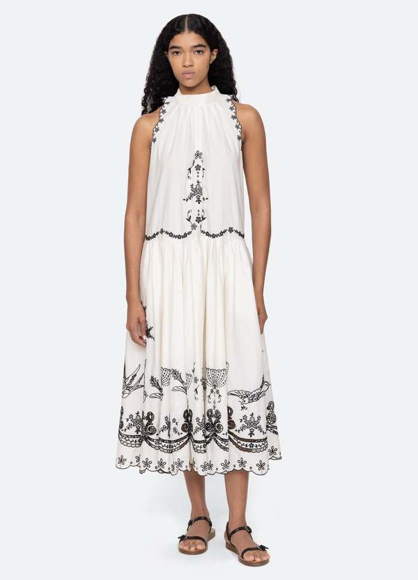 The Kingsley embroidered tank dress in cream by SEA NY showcases intricate embroidery throughout its design, offering a refined and elegant appeal. It features a high neckline that adds a sophisticated touch, complemented by a delicate back bow tie for adjustable fit and added charm. The scalloped hemline enhances the dress's feminine silhouette, making it an exceptional choice for those seeking a polished yet distinctive look.