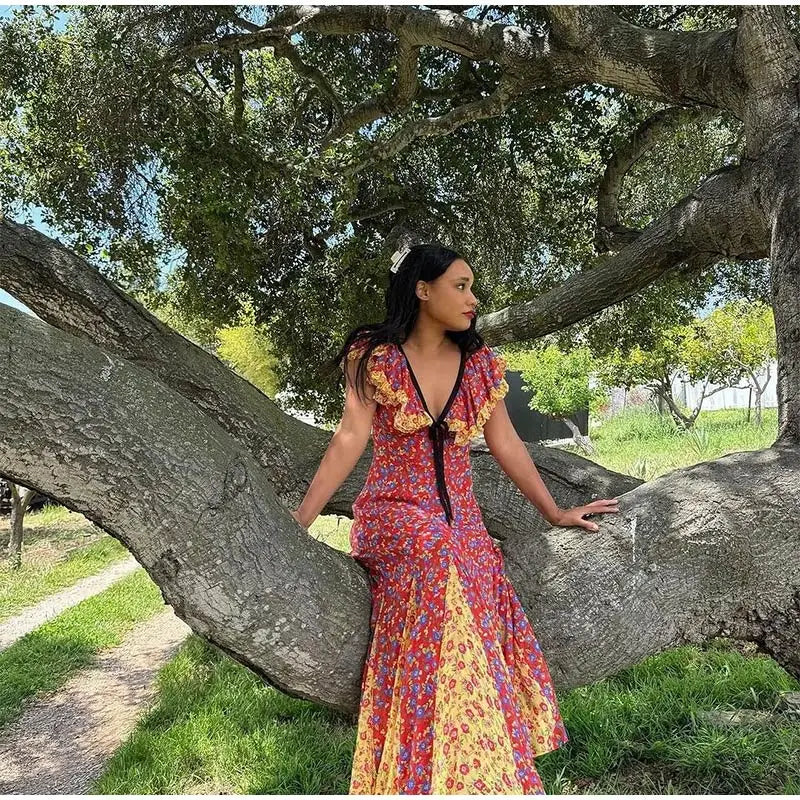 features a plunging V-neckline adorned with cascading picot-edged ruffles, a fixed grosgrain ribbon tie, and a viscose georgette lining. A fitted bodice with an invisible side zipper gives way to a flouncy full-length skirt with contrast godet panels.