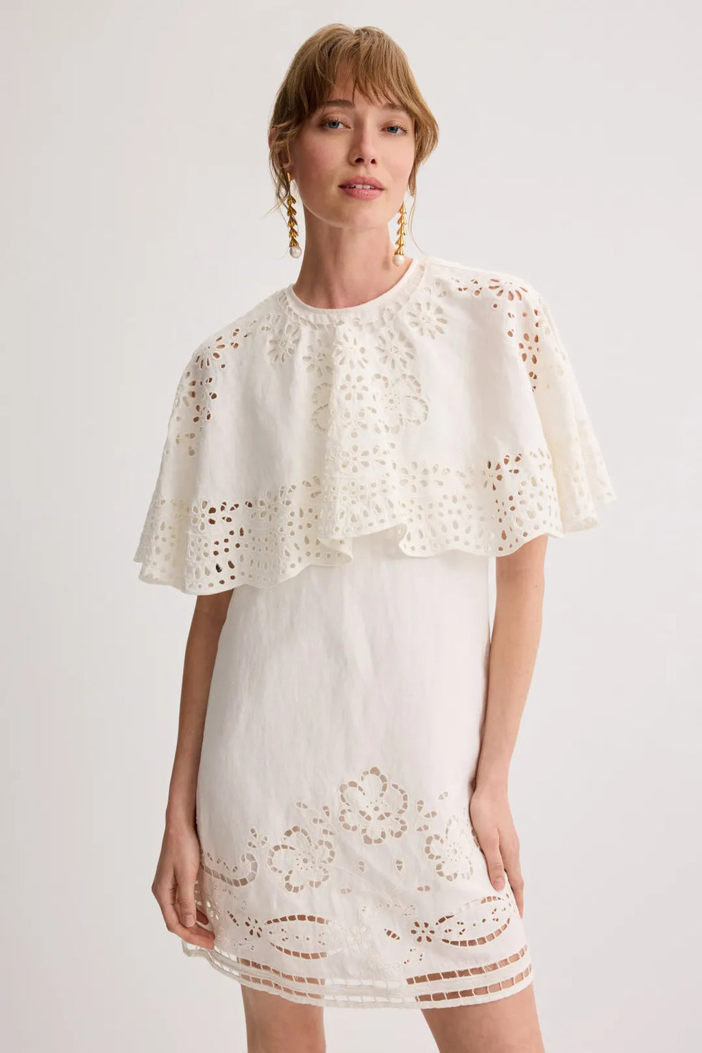 The Lula Mini Dress by Sea New York features intricate signature embroidery, complemented by a layered eyelet capelet and a delicate scalloped hem. This refined design effortlessly transitions from day to night. Pair it with leather ballet flats and a structured top handle bag to achieve a sophisticated, balanced look suitable for various occasions.