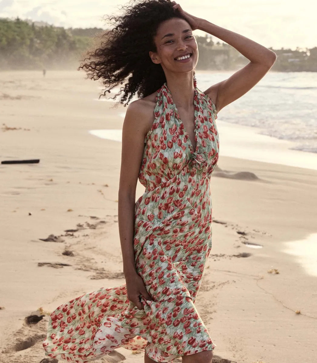 The Mazarin Dress in Tulip Fields by Doen exemplifies refined 1990s elegance with its buttery silk-viscose fabric and plunging halter neckline detailed with delicate ruffles. Featuring a fitted bodice and an invisible side zipper for a seamless fit, it also includes a removable silk georgette rosette brooch that adds versatile sophistication. 