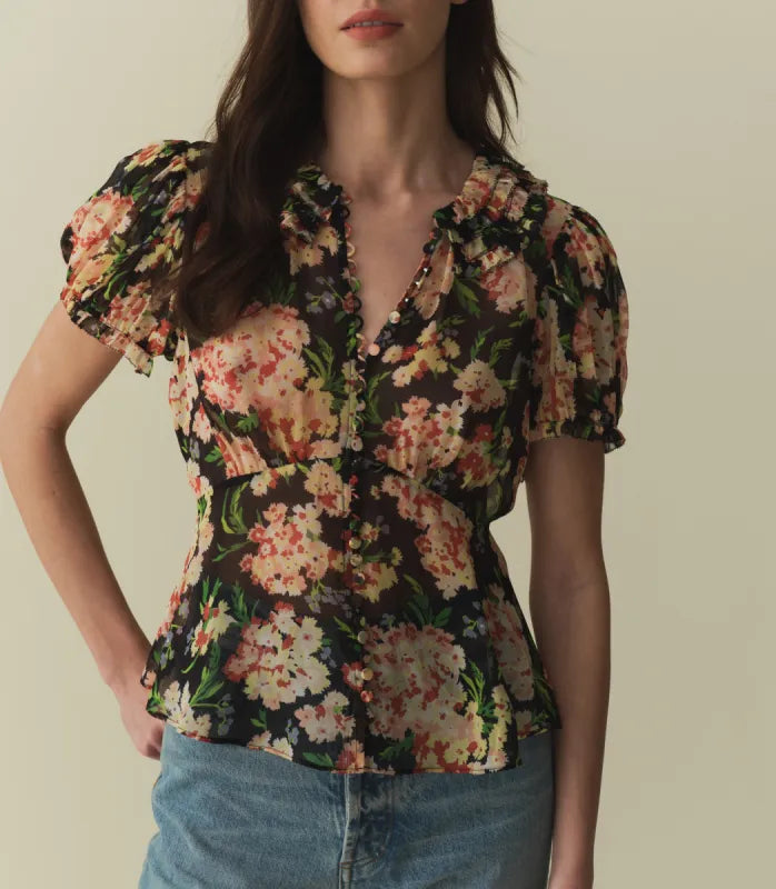 The Alona Top by Doen offers timeless sophistication with its light silk georgette fabric and 1930s-inspired design. Featuring short puffed sleeves and a Peter Pan collar adorned with delicate picot-edged ruffles, this blouse highlights a shirred bust that flows into a breezy, slightly cropped silhouette with a bias-cut hem. Self-covered buttons along the front enhance its refined charm. 